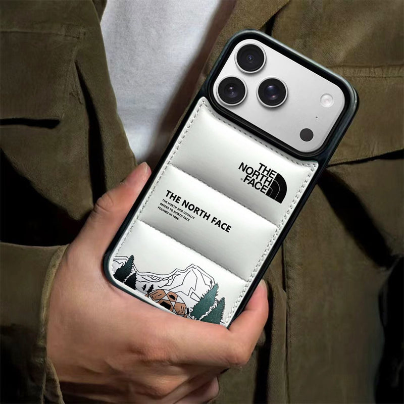 Hand holding a white quilted puffer phone case with a black camera module and mountain graphic illustration.